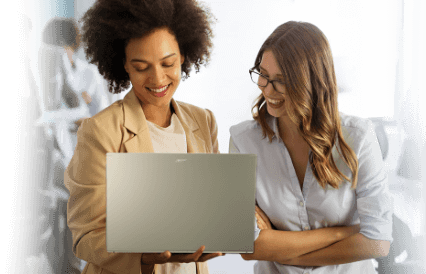 Uma das mulheres segura um notebook Acer enquanto a outra olha para a tela, ambas aparentam estar discutindo algo  relacionado ao conteúdo na tela do computador.