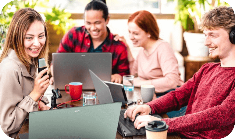 Amigos sentados à mesa, 2 homens e 2 mulheres sorrindo. Cada um está com um notebook Acer a sua frente na mesa.