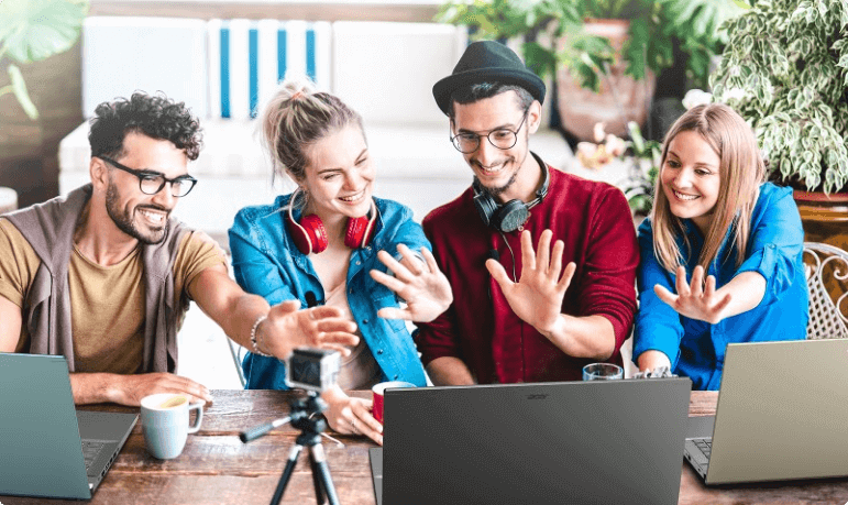 Amigos sentados à mesa, 2 homens e 2 mulheres acenando para um notebbok Acer Aspire 5 a sua frente.