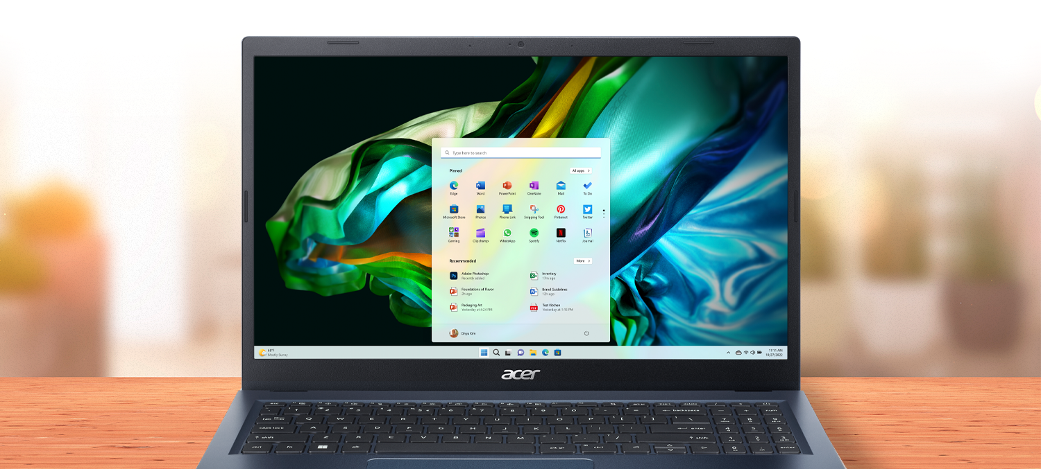 Notebook Acer Aspire 3 visto de frente com imagem abstrata em azul, verde e laranja na tela, sobre uma mesa.