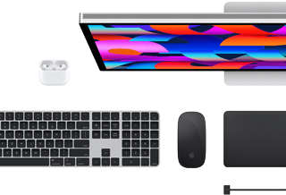 Imagem de cima dos acessórios para Mac: Studio Display, AirPods, Magic Keyboard, Magic Mouse e Magic Trackpad.