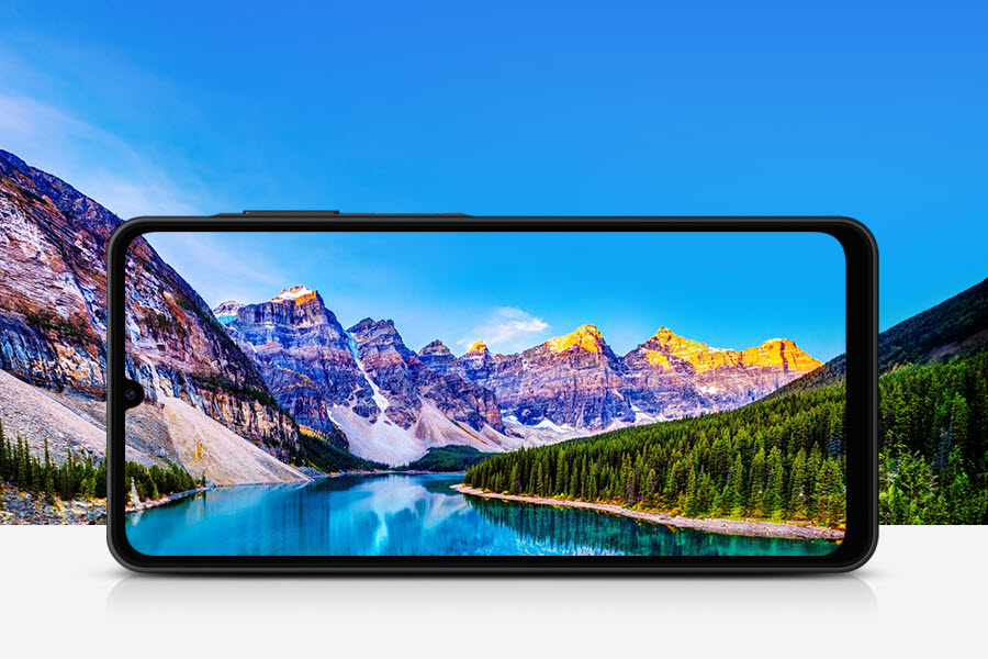 No fundo, um rio serpenteia entre montanhas rochosas e uma floresta em um dia ensolarado. Em primeiro plano, a tela de um Galaxy A06 5G posicionada horizontalmente enquadra a paisagem.